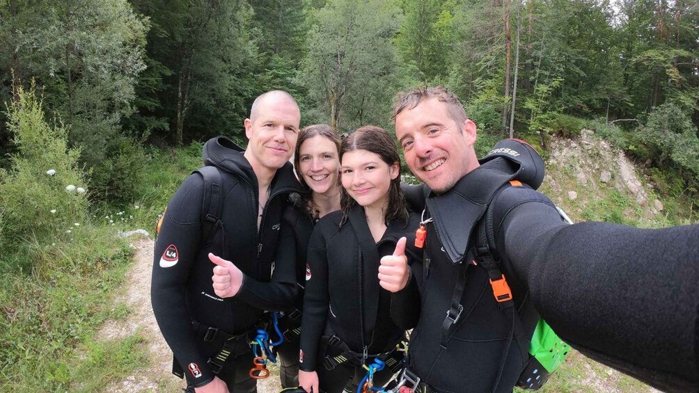 Four people in black wetsuits taking a selfie on a forest trail. 3