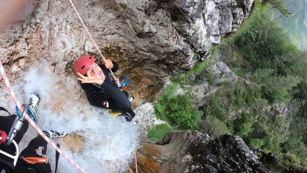 A person rappelling down a rocky cliff with a red helmet and harness. 1