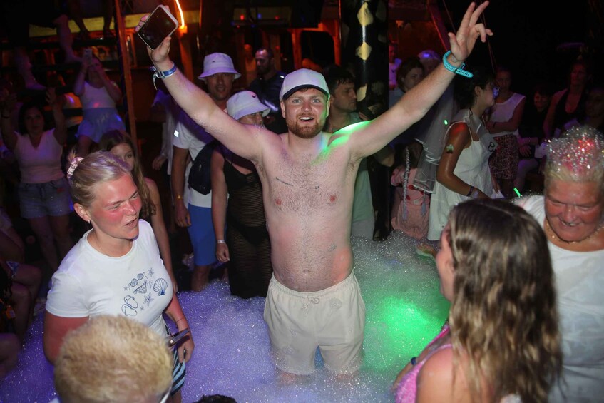 A person in a white cap and shorts, surrounded by people in a crowded indoor setting with a green light. 5