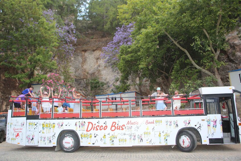 A bus with 'Disco Bus Music Book' written on its side, parked with passengers on the top deck. 1