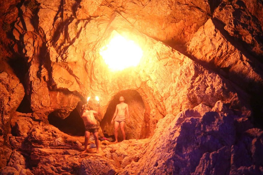 Two people standing in a cave with a bright light source above them. 3