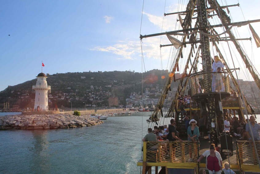 A coastal town with a lighthouse, a large sailing ship, and people on a dock. 4