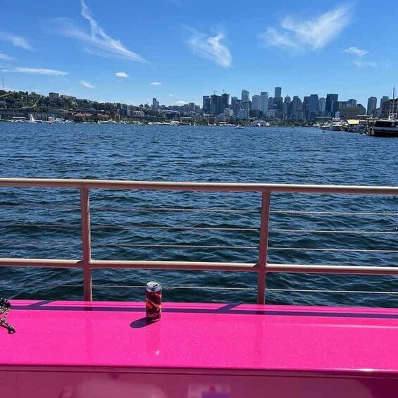 A pink boat with a can on the deck, water, and a city skyline in the background. 3