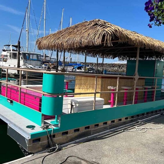 A colorful boat docked at a marina with a thatched roof, surrounded by other boats and a rocky shoreline. 1