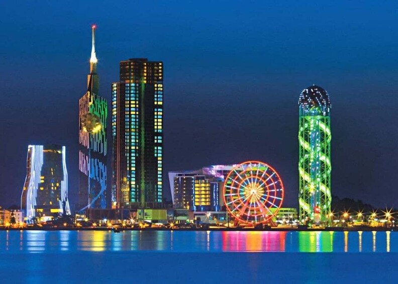 A city skyline at night with illuminated buildings, a Ferris wheel, and a water body reflecting the lights. 4