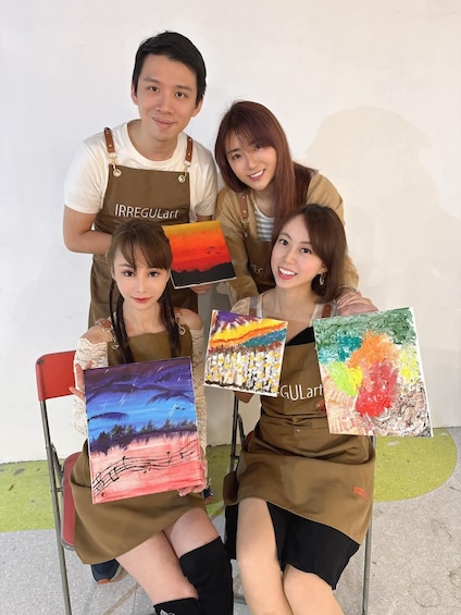 Four individuals holding colorful paintings, wearing aprons with 'IRREGULArt' and 'GULArt' logos. 1