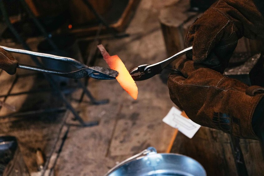 A person holding tongs over a glowing orange object, likely metal, in a workshop setting. 5
