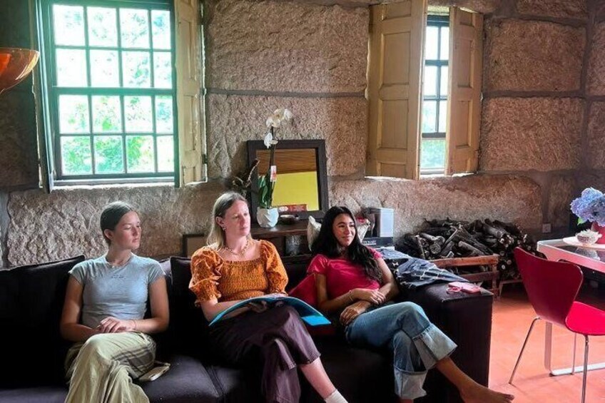 Three people sitting on a couch in a rustic room with stone walls and wooden shutters. 3