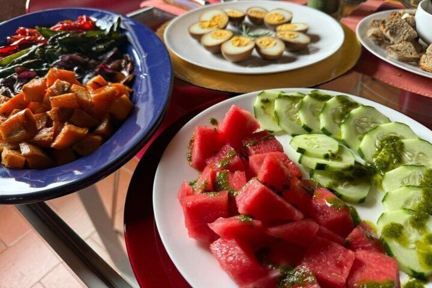 A table with plates of food including watermelon, cucumber, and a dish with cubed vegetables. 4