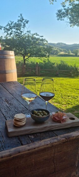 A wooden table with two glasses of wine, a bowl of olives, and a plate of cured meats. 5