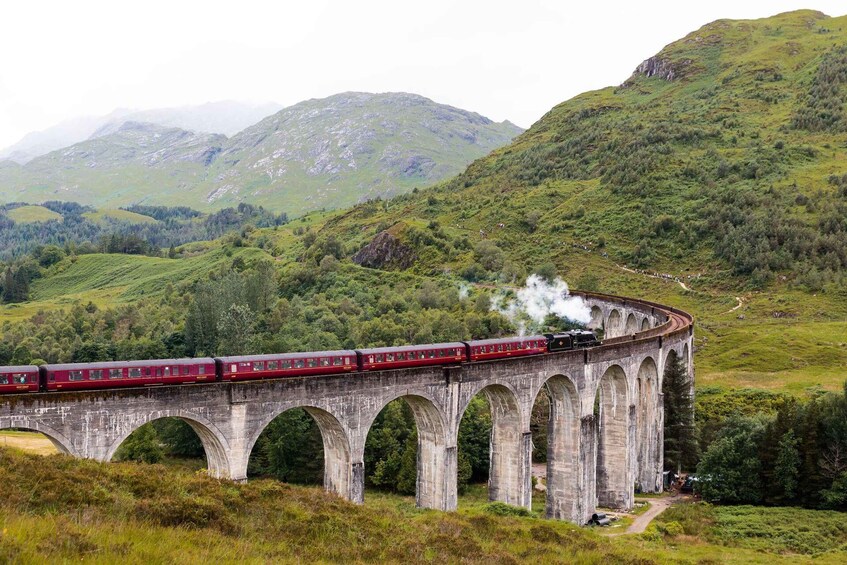 A red train traveling on a stone viaduct over a valley. 3
