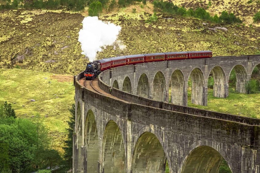 A steam locomotive crossing a stone viaduct over a grassy landscape. 2