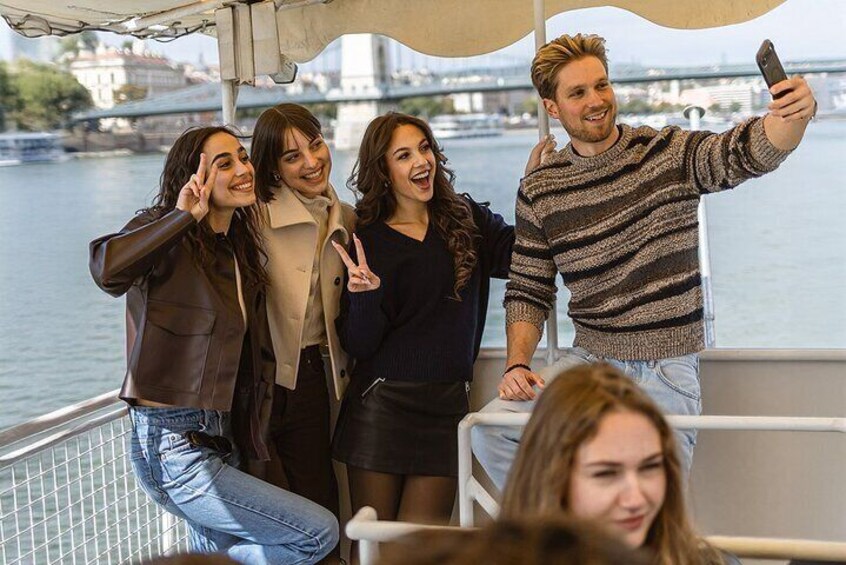 A group of people on a boat taking a selfie with a river and bridge in the background. 3