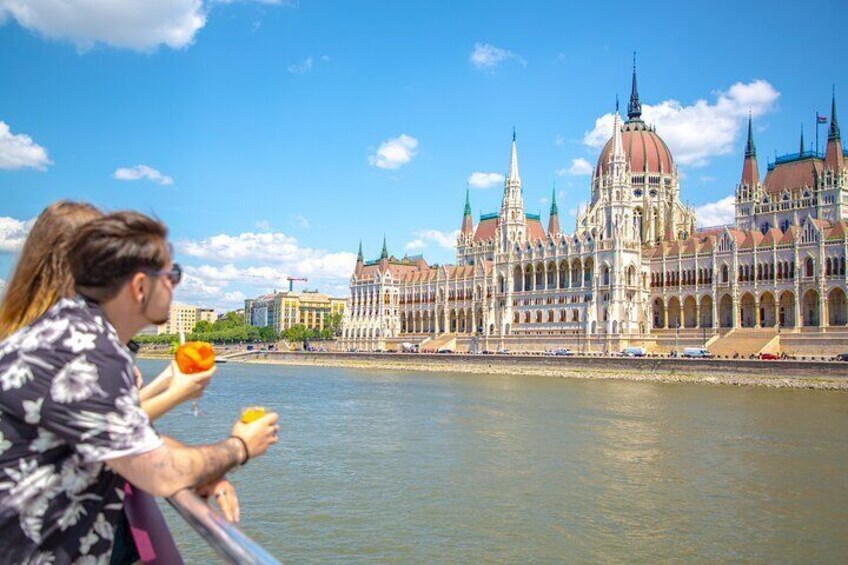 A person holding an orange by a river with a large, ornate building in the background. 5