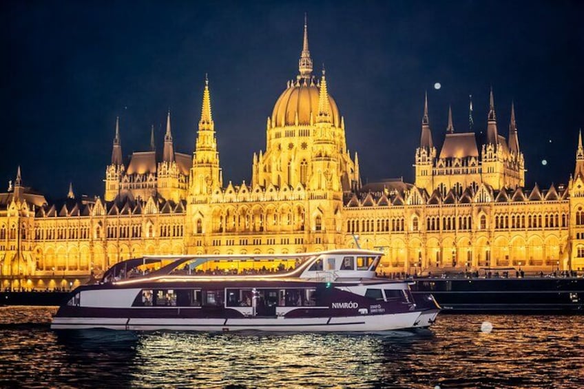 A boat with 'NIMROD' written on it, docked in front of a large, illuminated building with multiple spires. 3
