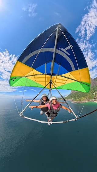 Two people paragliding over a coastal area with a clear sky and mountains in the background. 1