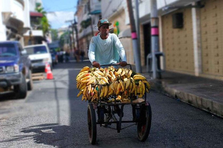 A person pushing a cart loaded with bananas down a street. 5