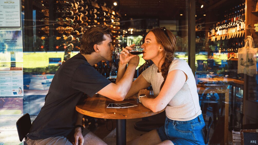 Two people sitting at a wooden table in a wine shop, with wine bottles in the background. 5