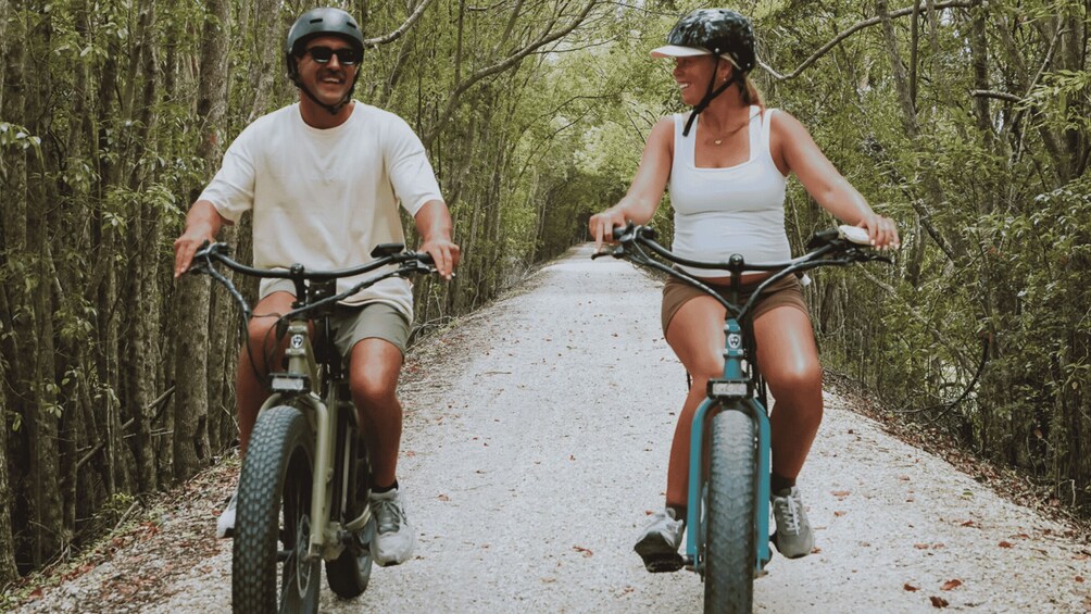 Two people riding bicycles on a gravel path surrounded by trees. 1