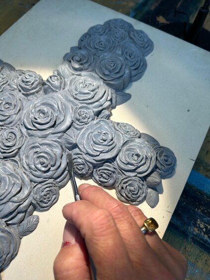 A person's hands sculpting gray roses on a white surface. 1