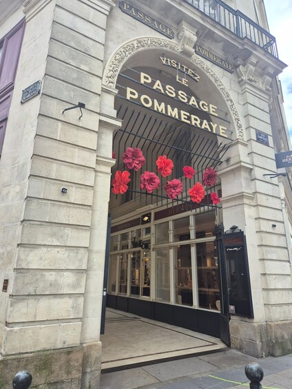 The entrance to Passage Pommeraye with ornate stonework and large red flowers. 3
