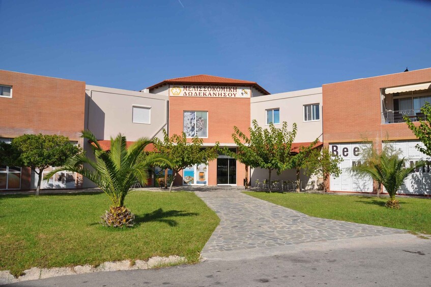 A modern building with a sign reading 'MEALIZOKOMIKH - ACADEMIZOHOS' and a large 'Bee' sign on the right. 3