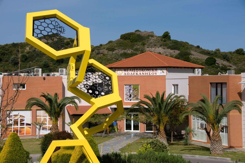 A yellow hexagonal sculpture with a bee design, palm trees, and a building with a red roof in the background. 2