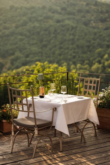 A table set outdoors with chairs, a tablecloth, and a scenic view of a forested hillside. 1