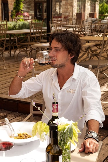 A person seated at an outdoor table with a bottle of wine, a glass, and a plate of food. 2