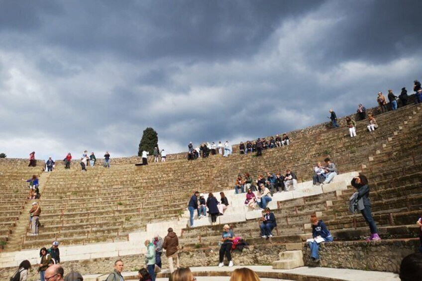 A stone amphitheater with people sitting and standing on the steps. 3