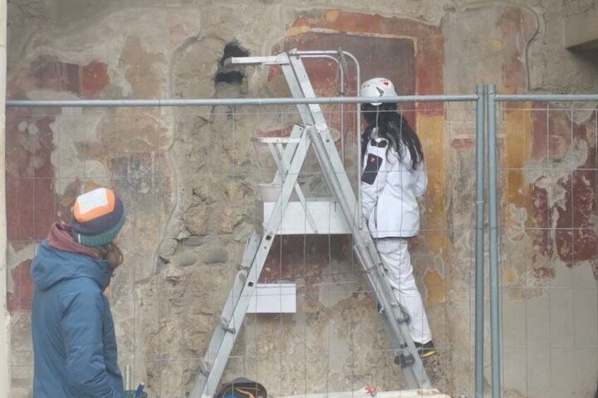 A person on a ladder working on a wall, another person observing, and a metal ladder. 4