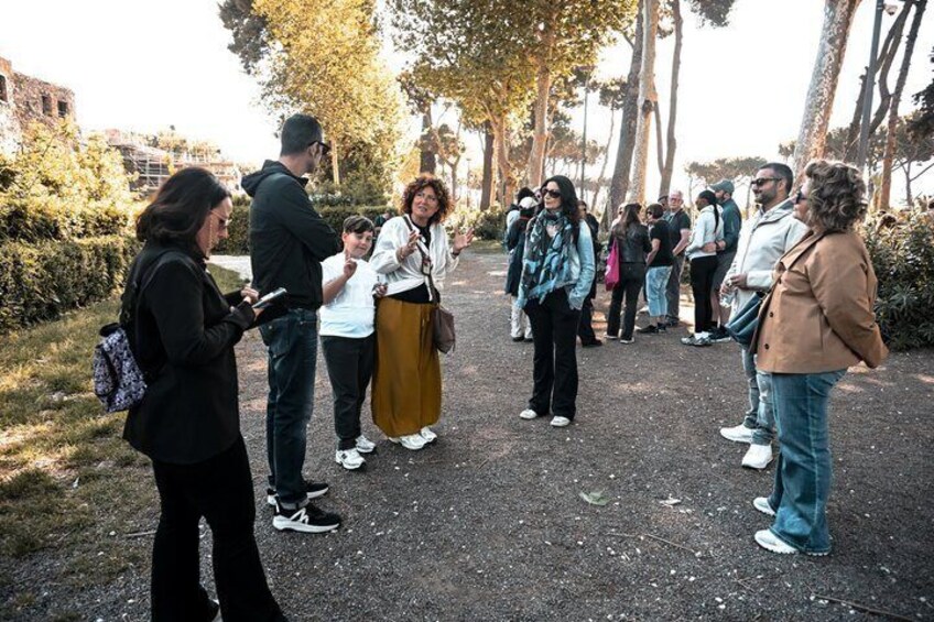 A group of people standing on a paved path in a park with trees and grass around. 1
