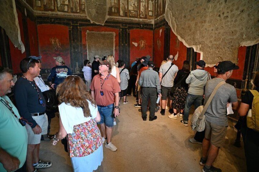 A group of people inside a historical building with red walls and a patterned ceiling. 2