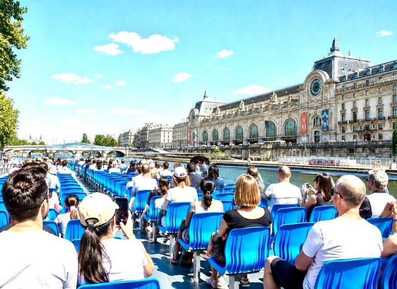 People seated on blue chairs facing a river with a historic building in the background. 2