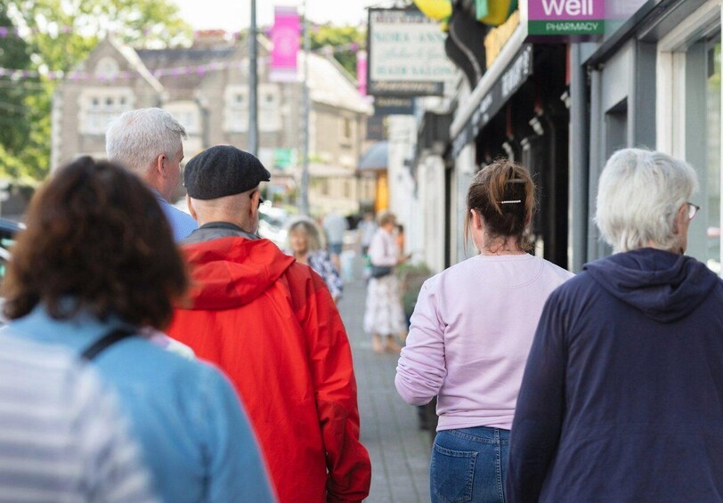 A group of people walking on a sidewalk in an urban area with storefronts and a pharmacy sign. 4