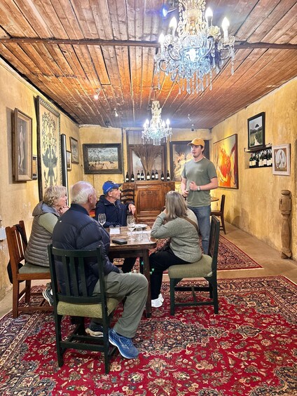 A group of people seated around a table in a room with wooden ceilings, a chandelier, and various framed artworks on the walls. 4