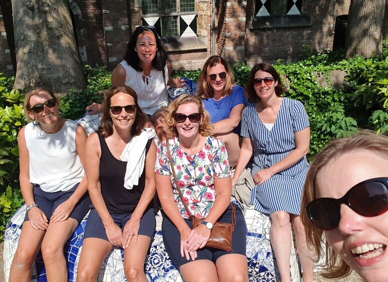 A group of people sitting on a patterned bench in a garden with brick walls and greenery. 2