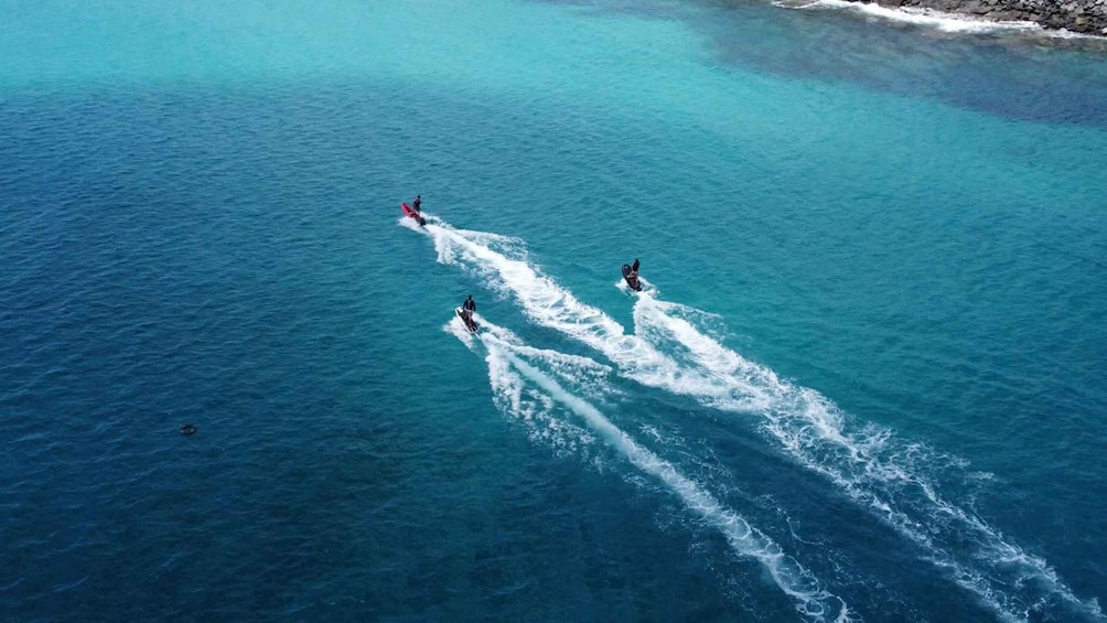 Three jet skis creating wake trails in turquoise ocean water. 3