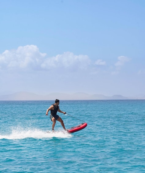 A person wakeboarding on a clear day over turquoise water with distant mountains. 1