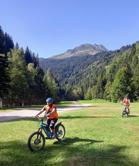 Two cyclists on a grassy field with a mountainous backdrop. 2