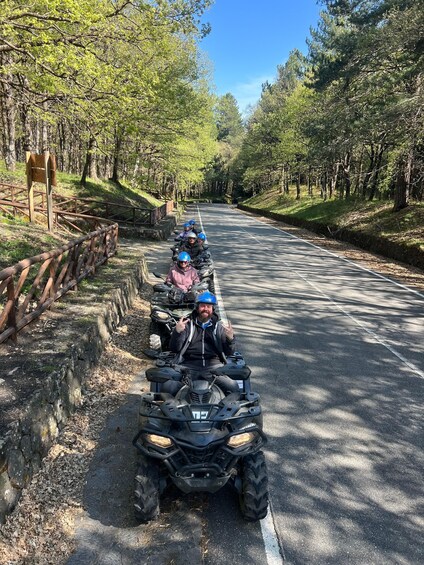 A group of people on ATVs on a paved road surrounded by trees. 2