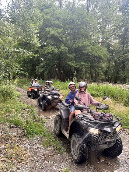 Four people on ATVs on a dirt trail surrounded by trees. 5