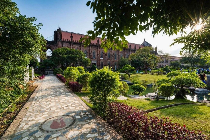 A stone pathway leading to a historic building with a red roof, surrounded by lush greenery and a small pond. 4