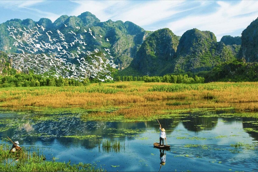 A person standing on a boat in a calm water body surrounded by lush greenery and mountains. 1