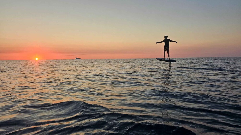 A person surfing on a wave at sunset with a boat in the background. 1