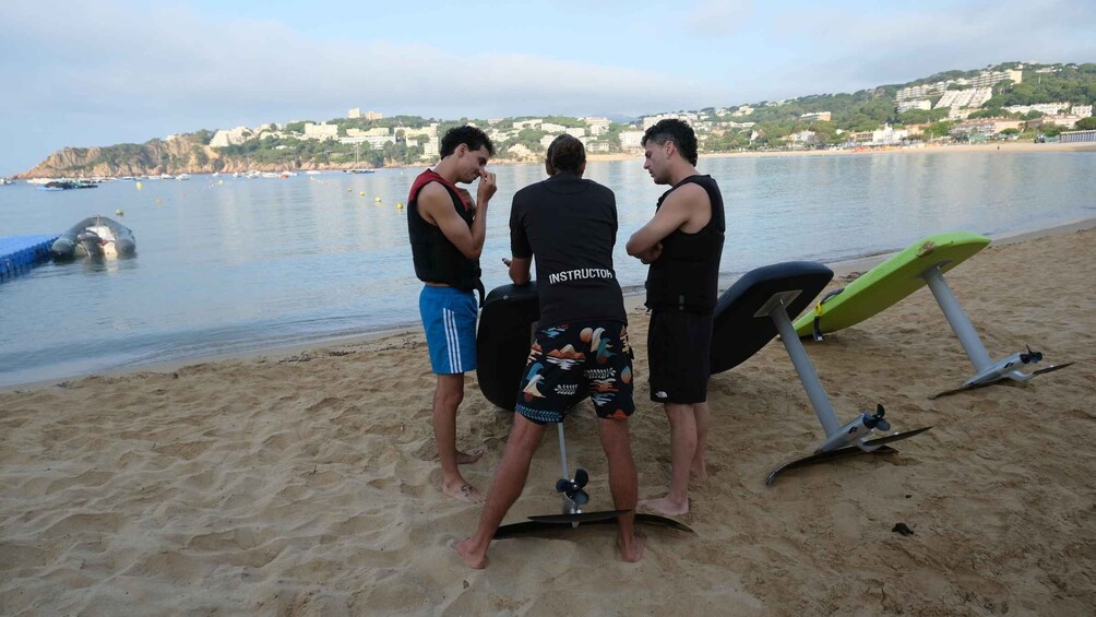 Three people on a sandy beach with a water body and boats in the background. 5