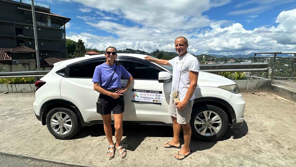Two people standing beside a white car with a sign on the side. 5