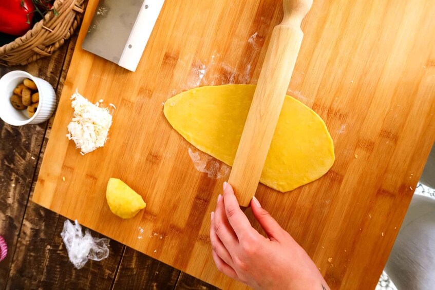A person rolling dough on a wooden surface with a rolling pin, a knife, and a bowl of nuts nearby. 2