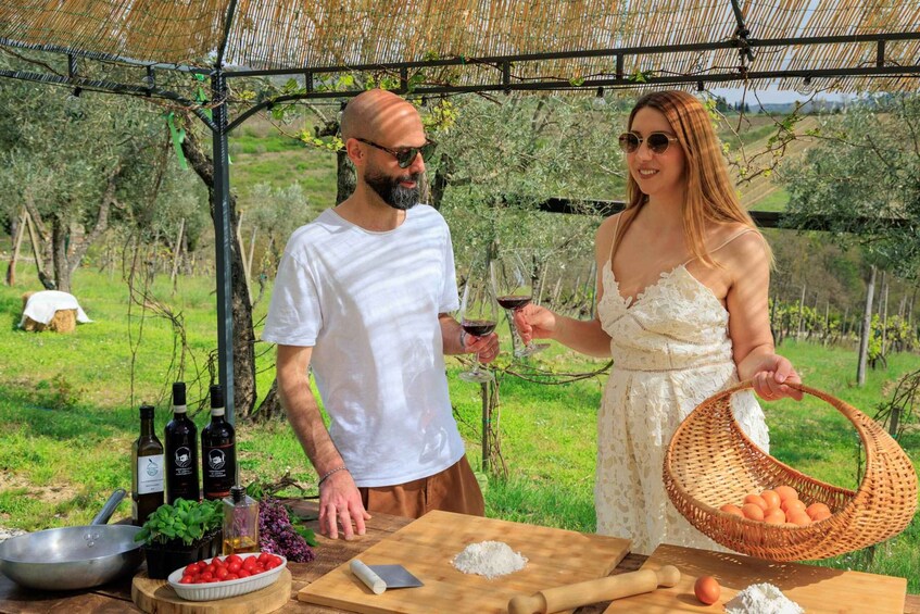 Two people outdoors with wine bottles, a basket of eggs, and a table with food items. 5