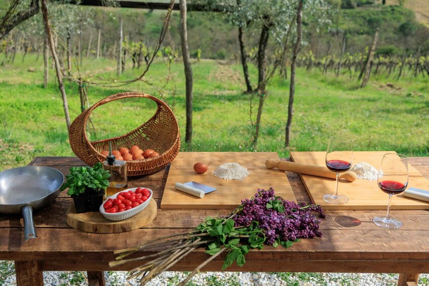 A picnic table with food, wine, and a basket of eggs in a vineyard setting. 3